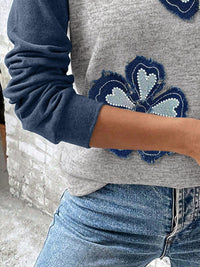 Person wearing a gray sweater with blue floral patterns and blue jeans.