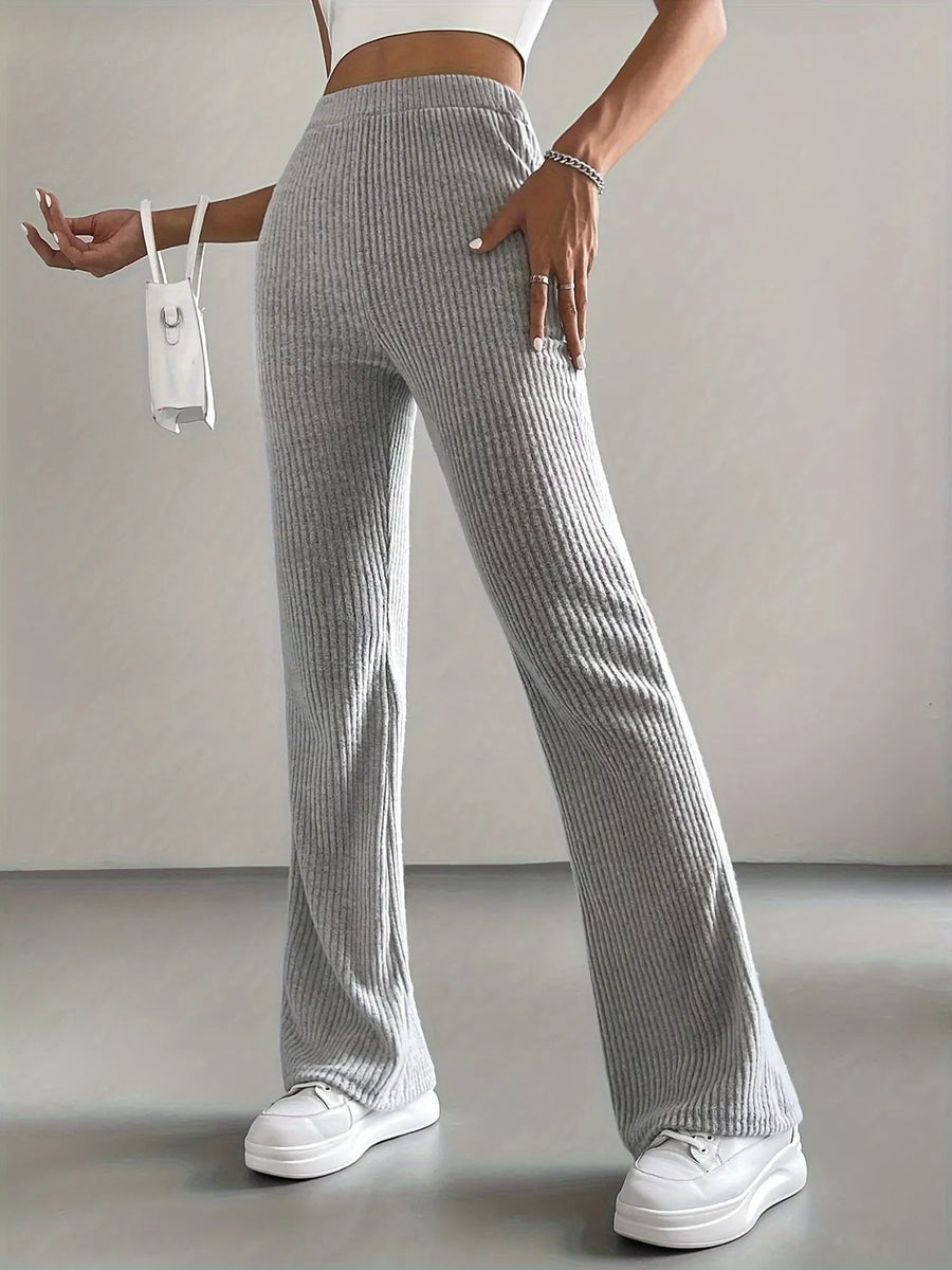 Person wearing gray ribbed pants and white sneakers on a plain background