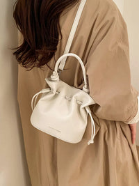 Person wearing a beige coat with a white drawstring bag over their shoulder.