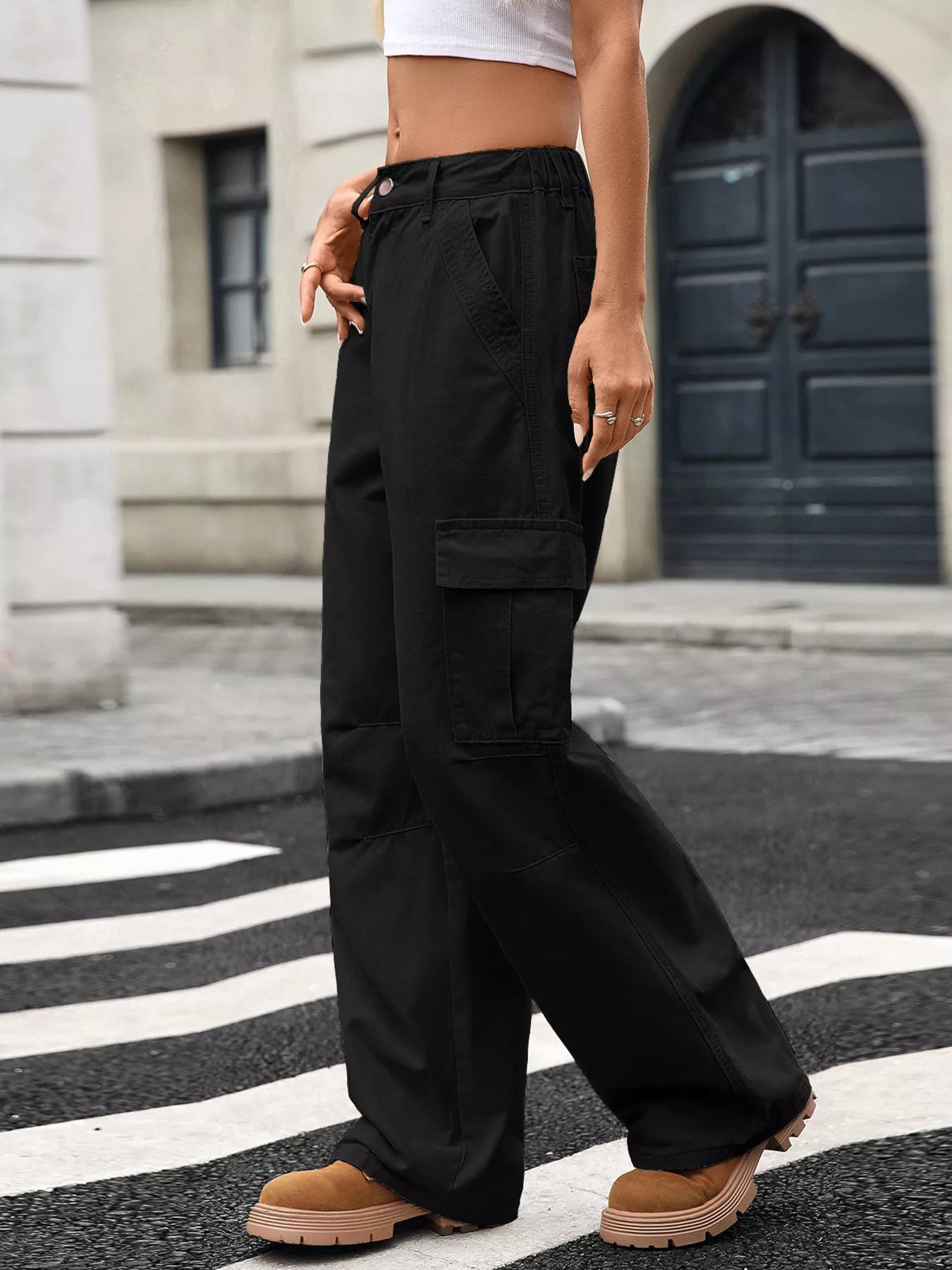 Person wearing black cargo pants on a street with a building in the background