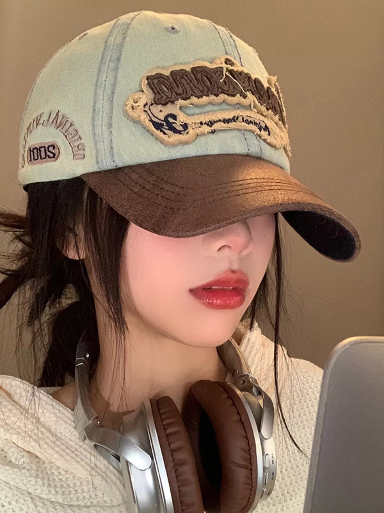 Person wearing a denim cap with embroidery and headphones, against a neutral background