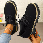 Black lace-up shoes being held up with a neutral background