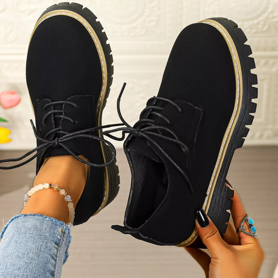 Black lace-up shoes being held up with a neutral background