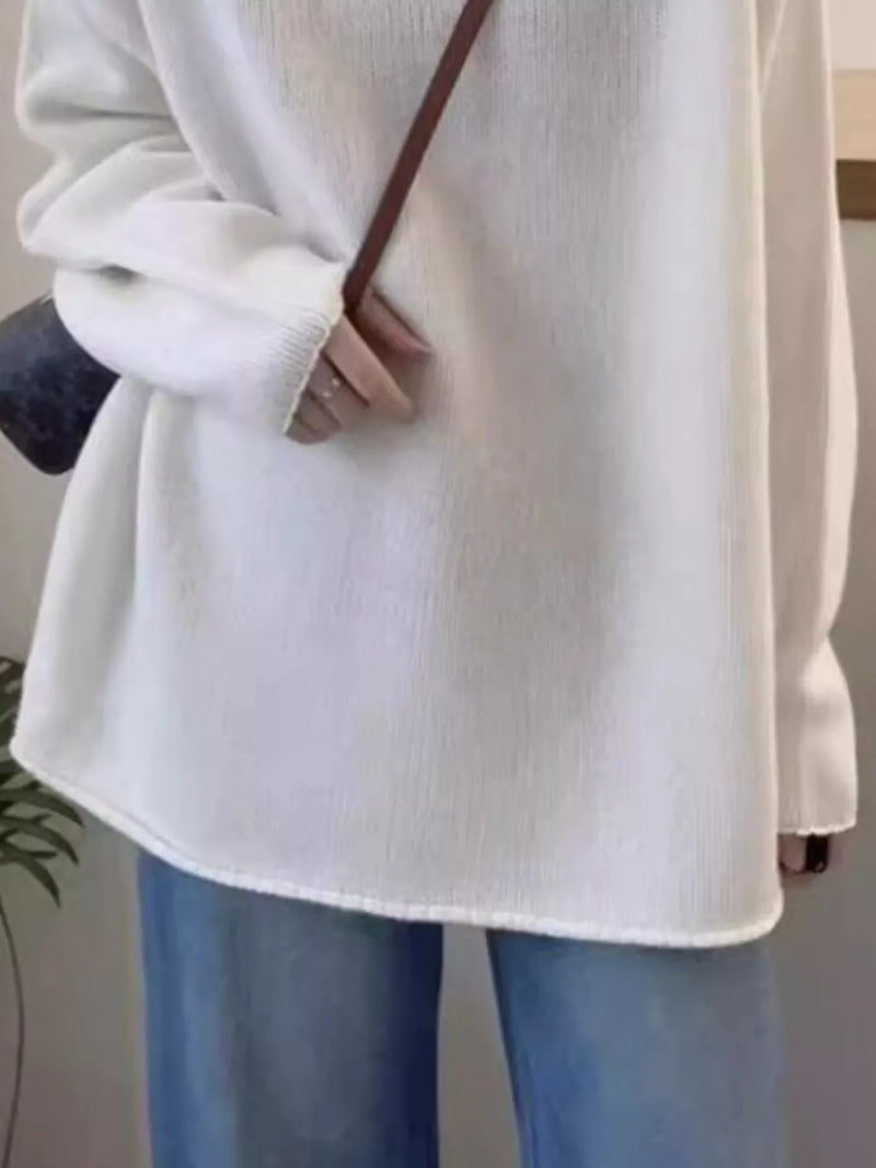 Person wearing a white sweater and blue jeans with a blurred background