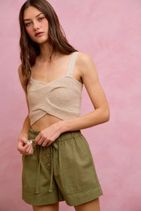 Woman wearing a beige top and green shorts against a pink background