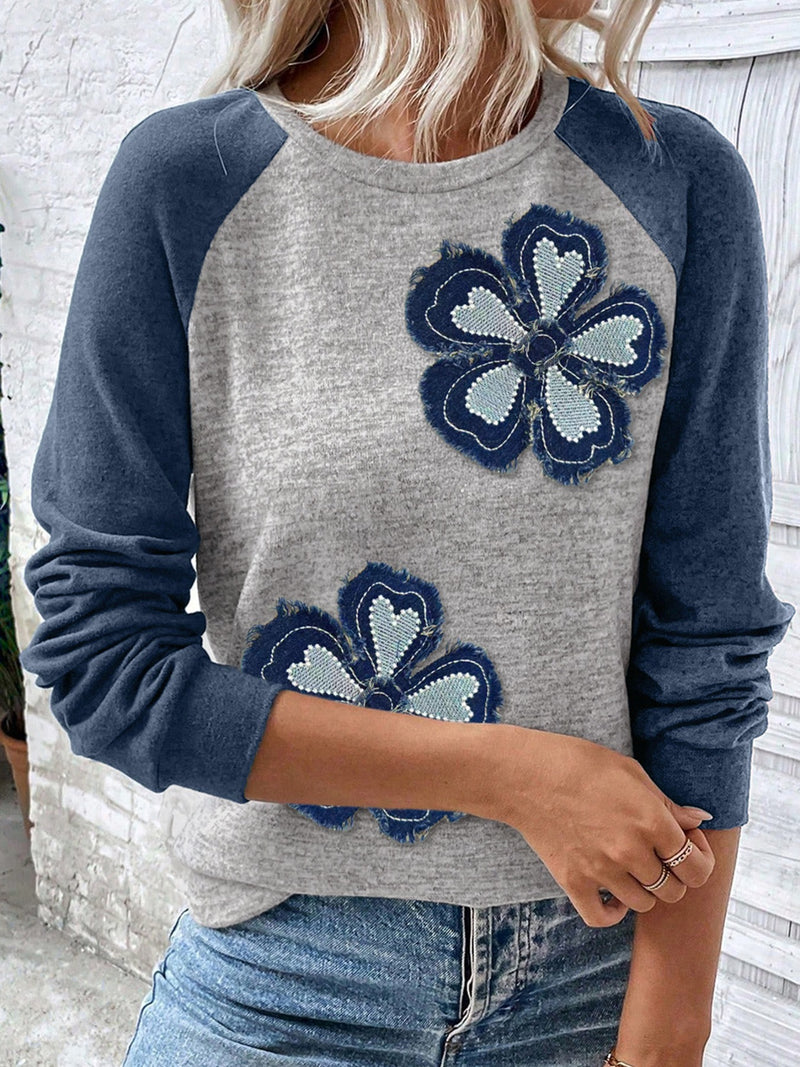 Gray sweater with blue sleeves and floral patterns worn by a person.