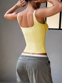 Person wearing a yellow tank top and gray pants against a neutral background