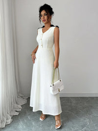 Woman in a white dress holding a white handbag against a gray curtain background