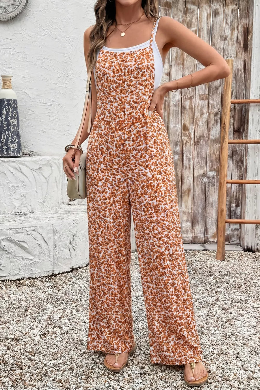 Woman wearing a floral jumpsuit standing in front of a wooden wall.