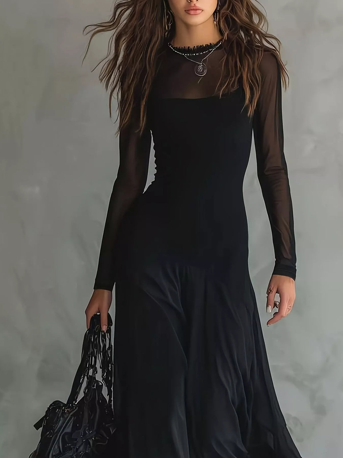 A woman models a black long-sleeve maxi dress with sheer mesh sleeves and a square neckline, holding a black handbag against a textured gray background.