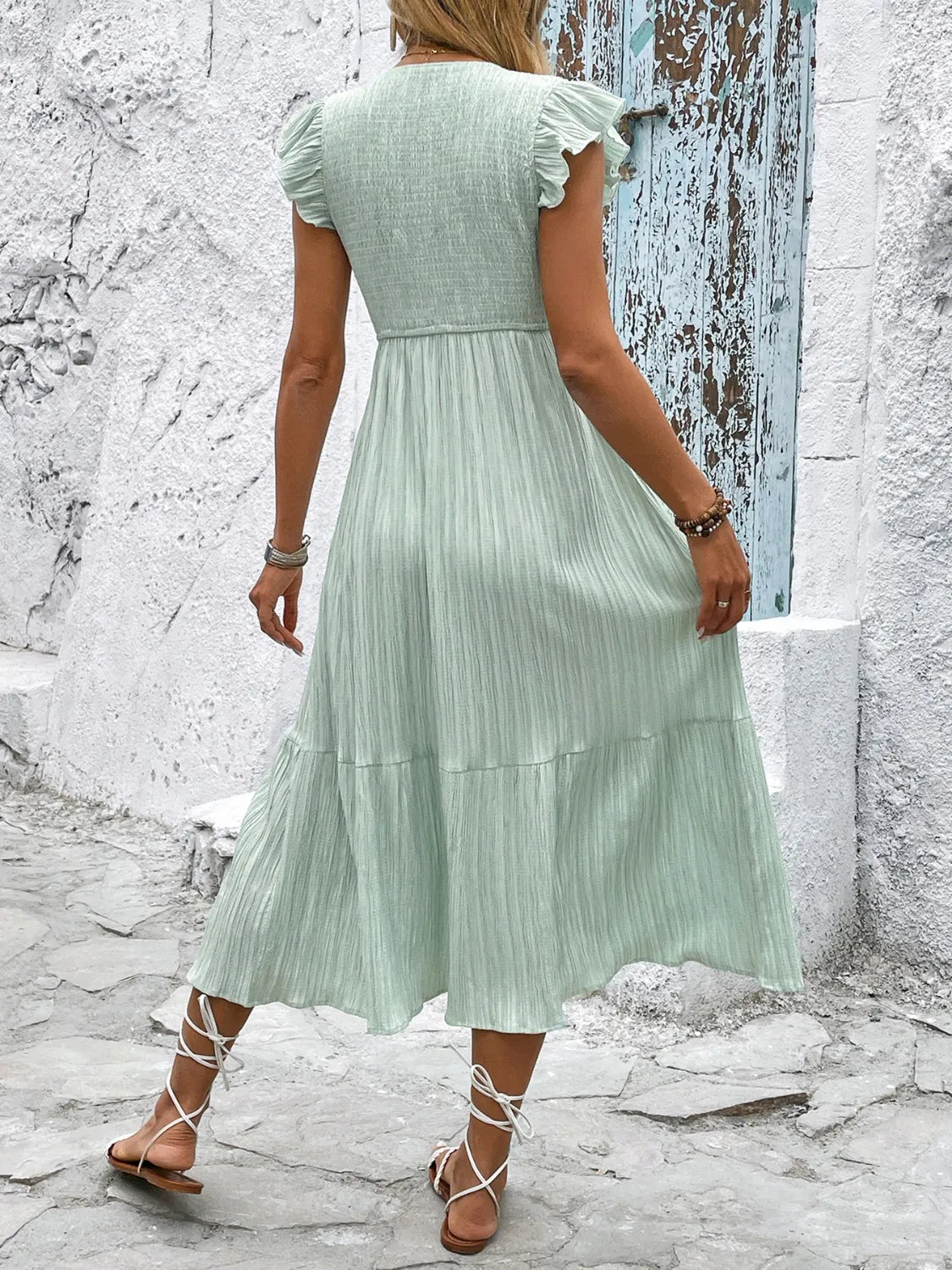 Woman wearing a light green dress standing against a textured wall.