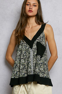 Woman wearing a sleeveless top with floral pattern and black trim against a plain background
