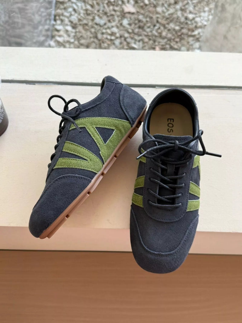 Pair of navy blue sneakers with green accents on a wooden surface.