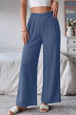 Person wearing blue wide-leg pants and a white top in a bedroom setting.
