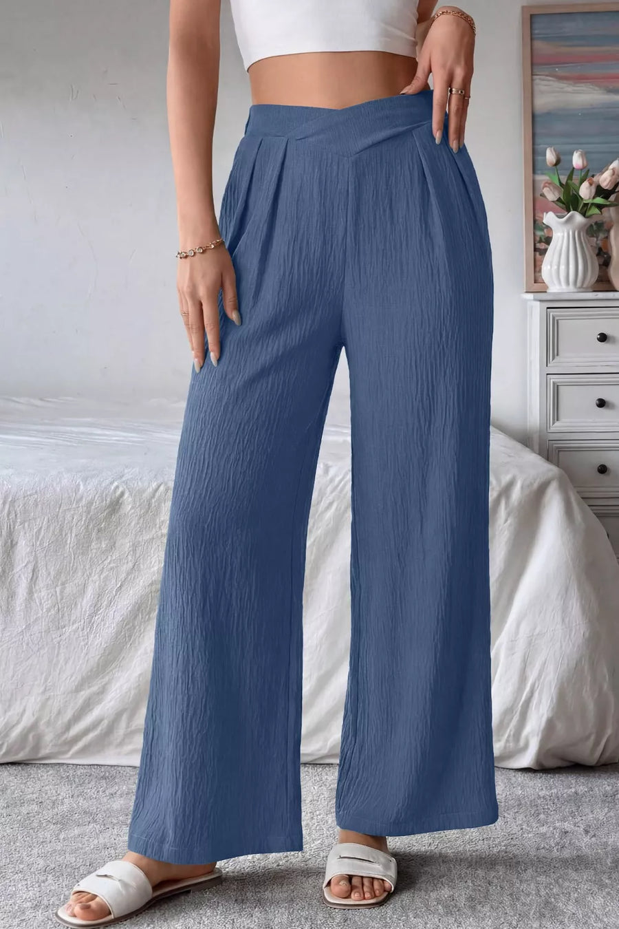 Person wearing blue wide-leg pants and a white top in a bedroom setting.