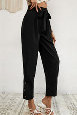 Black pants with a tie waist worn by a person on a white background
