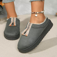 Gray slippers with tassels worn by a person on a textured surface
