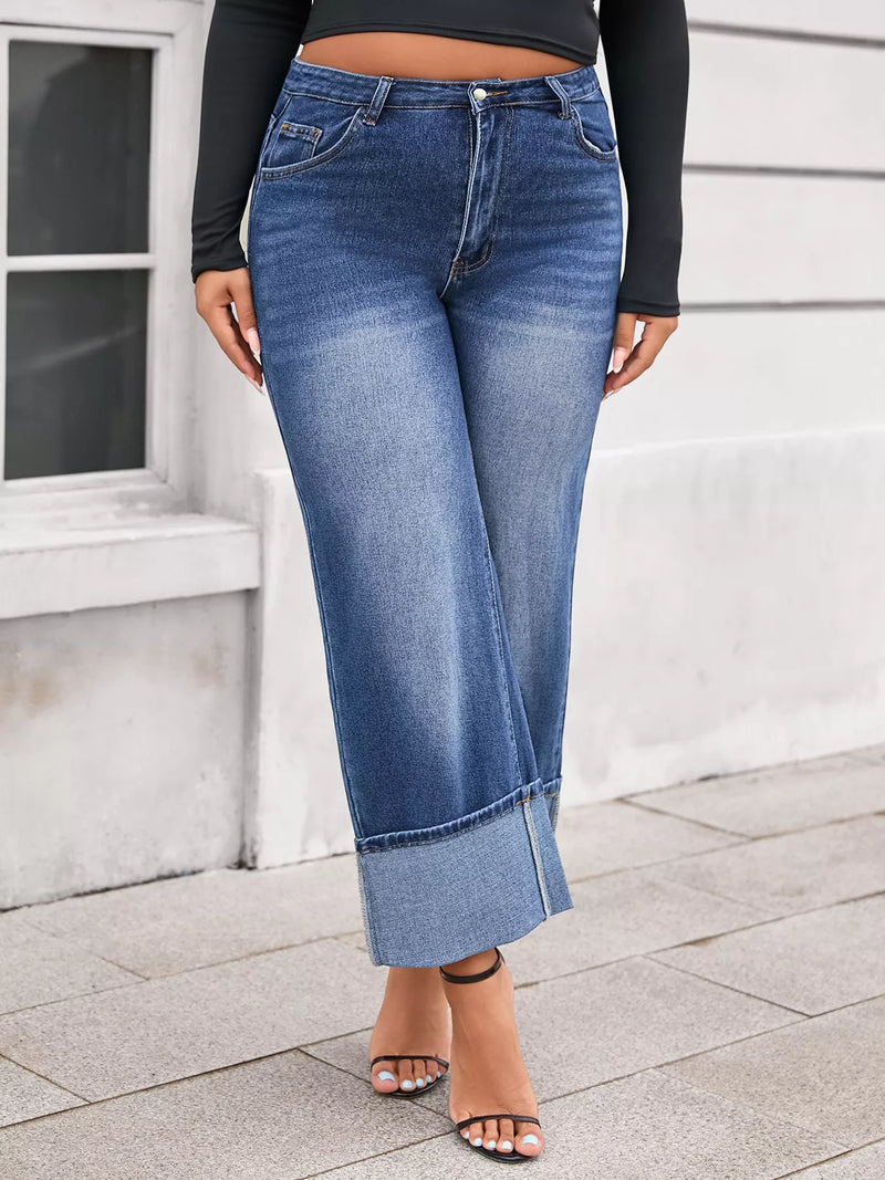 Person wearing blue jeans and a black top standing on a sidewalk.