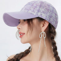 Woman wearing a purple plaid cap and pearl earrings on a white background