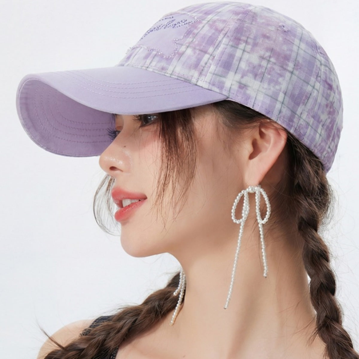 Woman wearing a purple plaid cap and pearl earrings on a white background