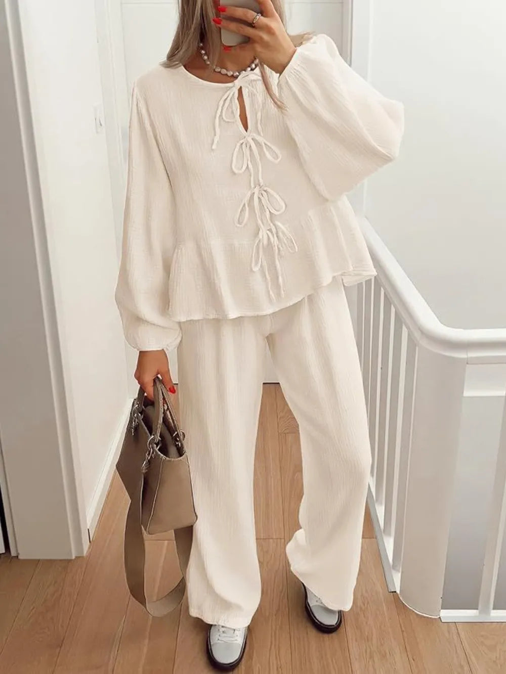 Person wearing a white outfit with a matching handbag indoors.