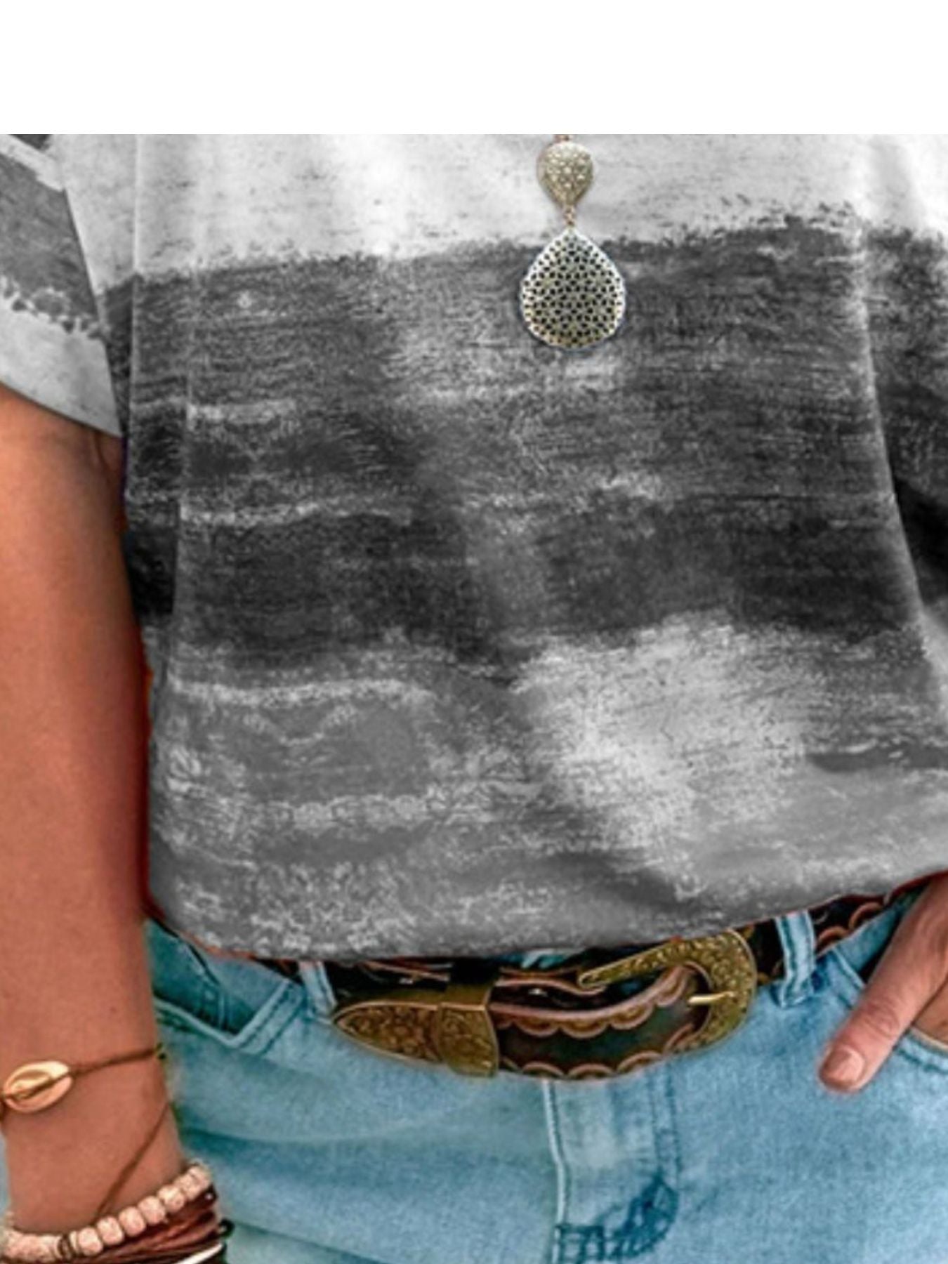Person wearing a gray t-shirt with a patterned pendant, light blue jeans, and a decorative belt.