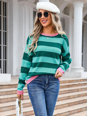 Woman wearing a green and pink striped sweater with jeans and a white hat, standing on steps.