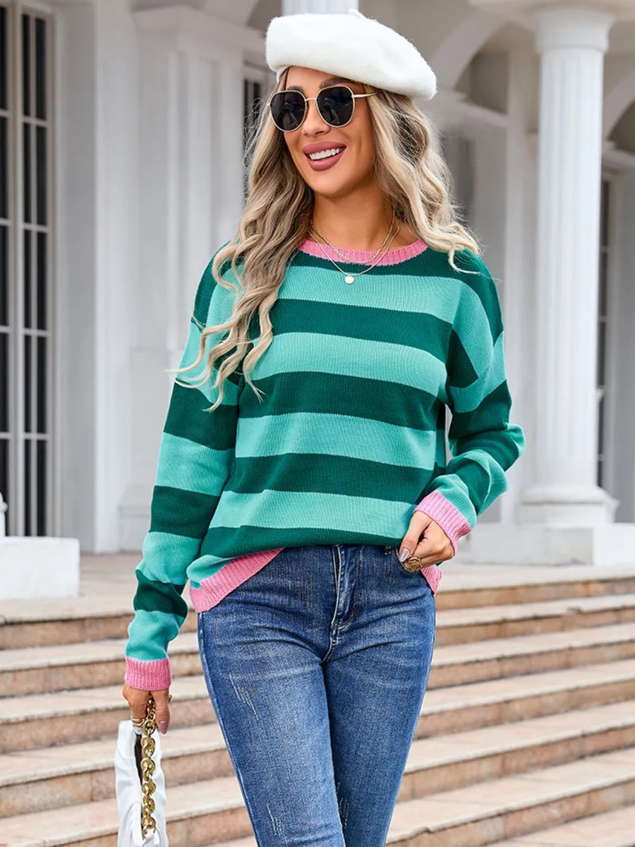 Woman wearing a green and pink striped sweater with jeans and a white hat, standing on steps.