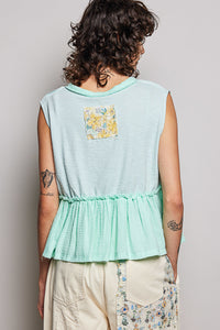 Person wearing a light blue sleeveless top with a floral pocket on a plain background