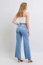 Woman wearing light blue jeans and a white top on a plain background