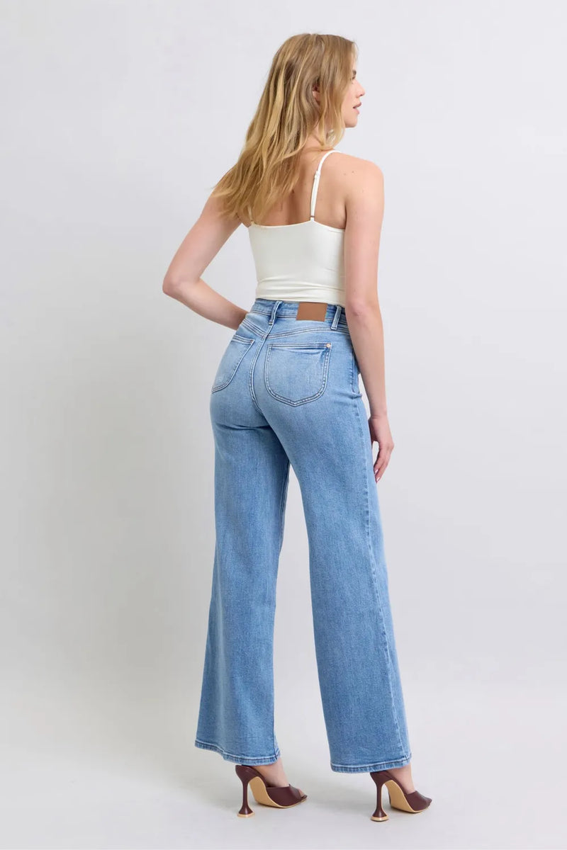 Woman wearing light blue jeans and a white top on a plain background