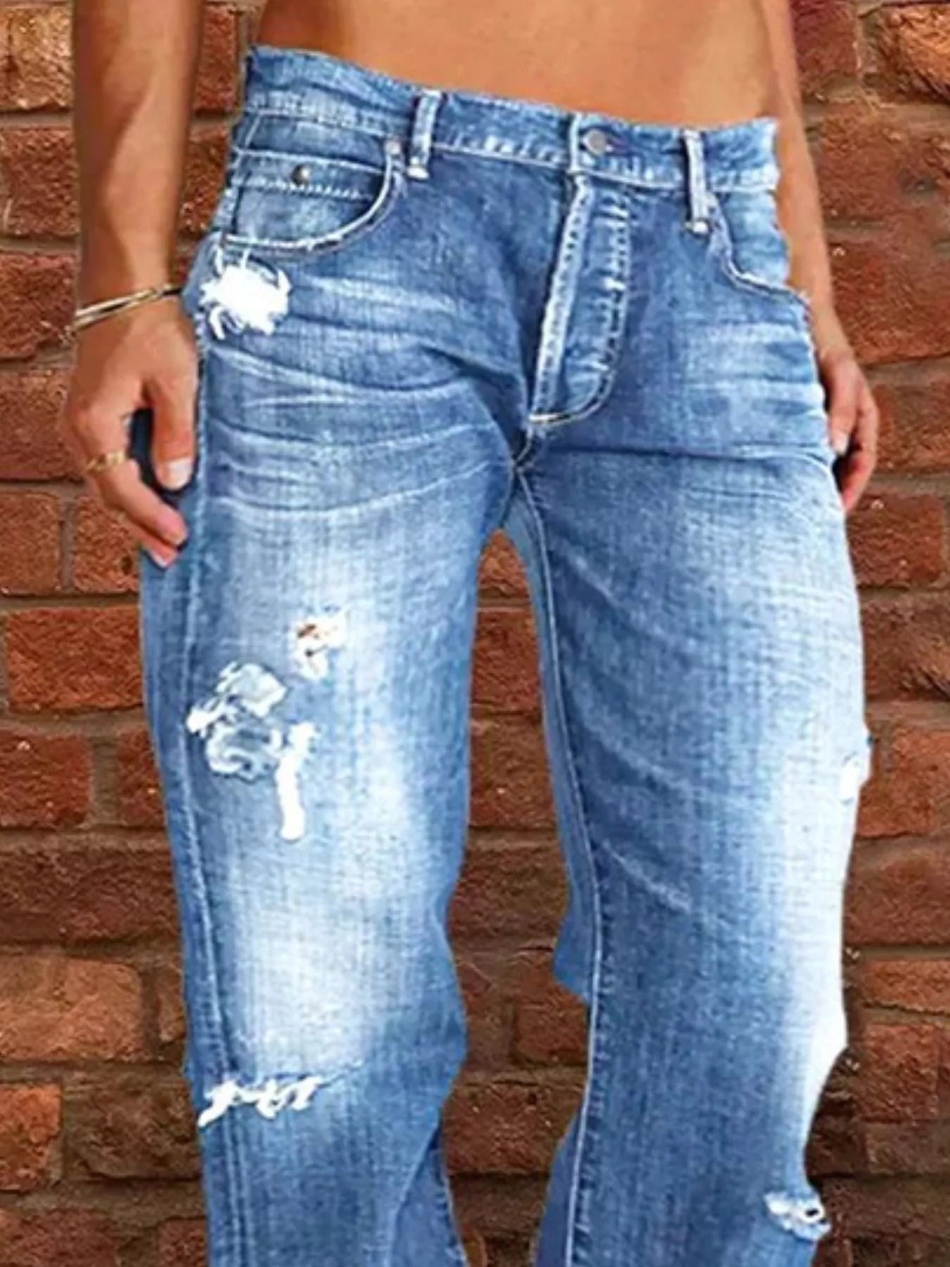 Distressed blue jeans worn by a person against a brick wall.