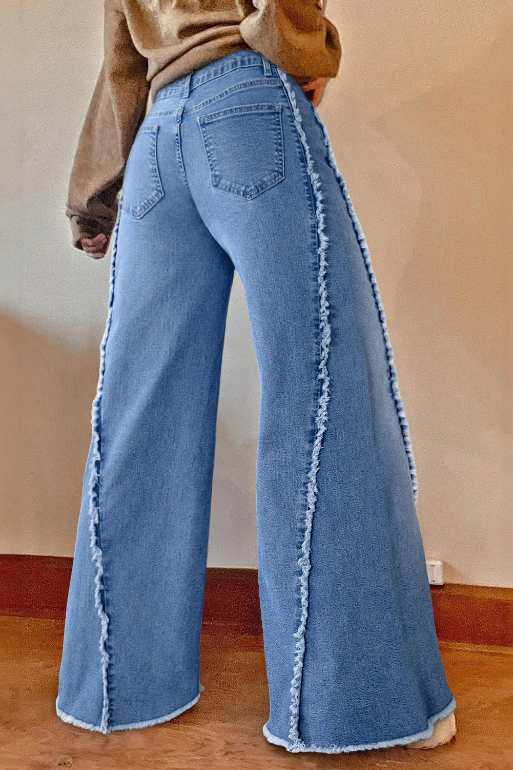 Blue jeans with frayed edges worn by a person on a plain background