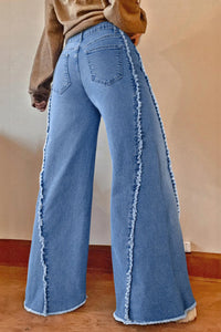 Blue jeans with frayed edges worn by a person on a plain background