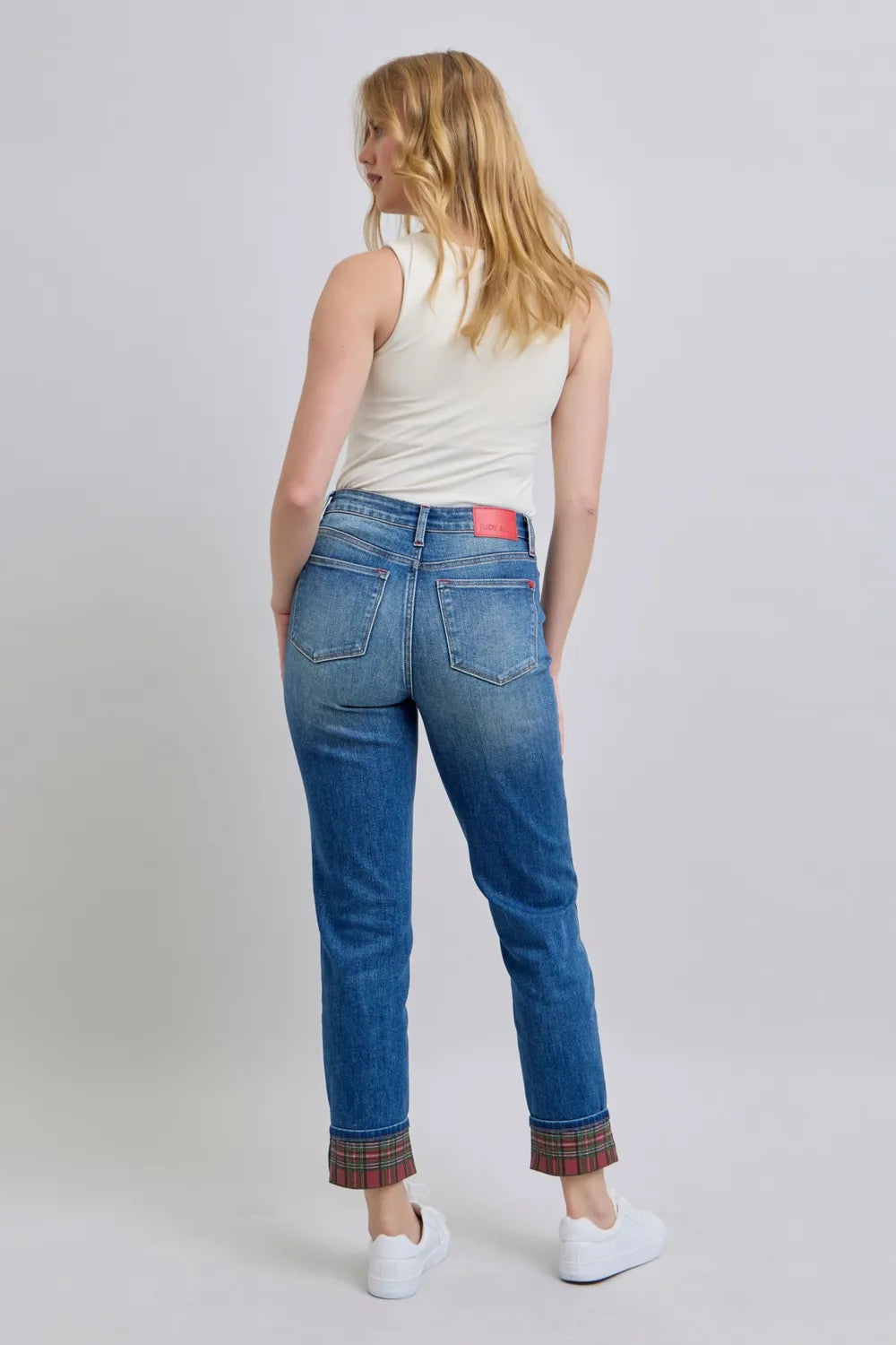 Woman wearing blue jeans with a red tag on a plain background