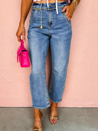Person wearing high-waisted blue jeans with a pink background