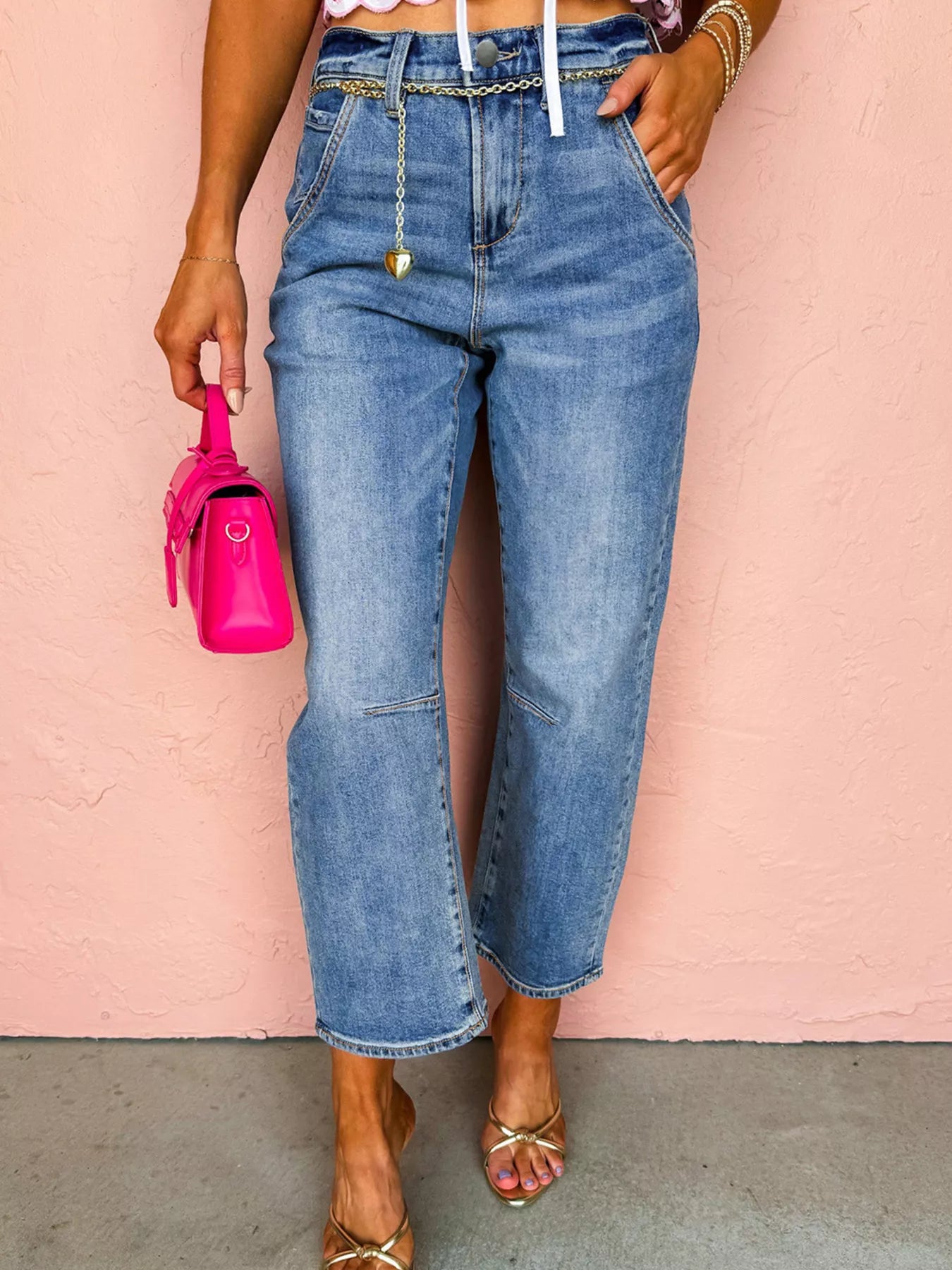 Person wearing high-waisted blue jeans with a pink background