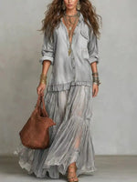 Woman in a flowing gray dress holding a brown bag against a neutral background