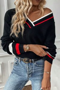 Person wearing a black sweater with red and white stripes and blue jeans.