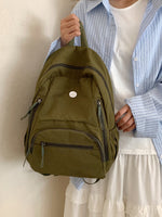 Person holding a green backpack against a neutral background