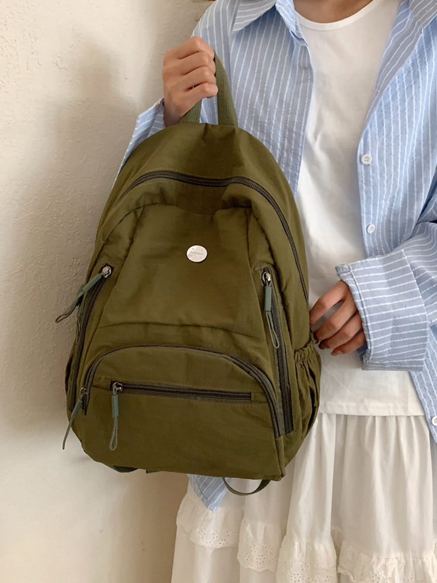 Person holding a green backpack against a neutral background