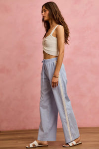 Woman wearing a white top and light blue checkered pants with a pink background