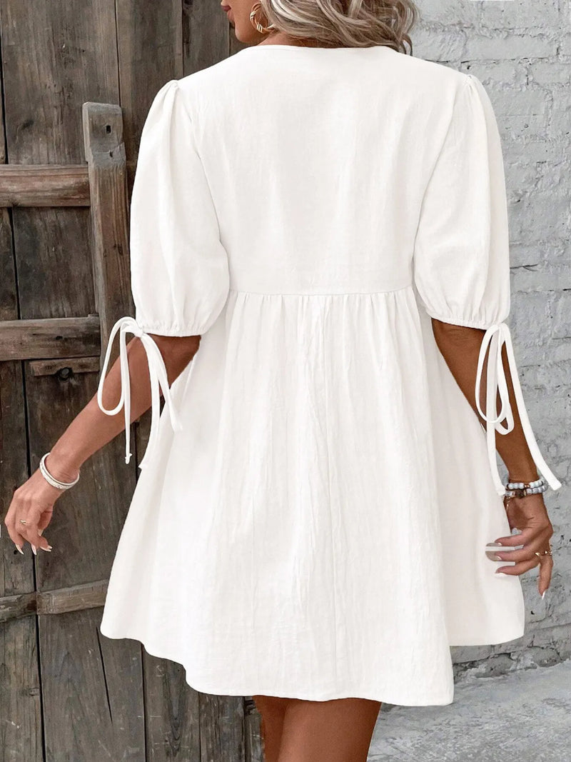 Woman wearing a white dress with tie sleeves against a wooden and stone wall.
