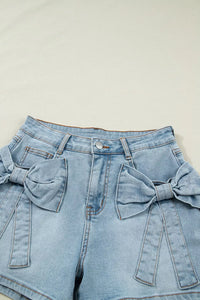 Light blue denim shorts with bow details on a beige background