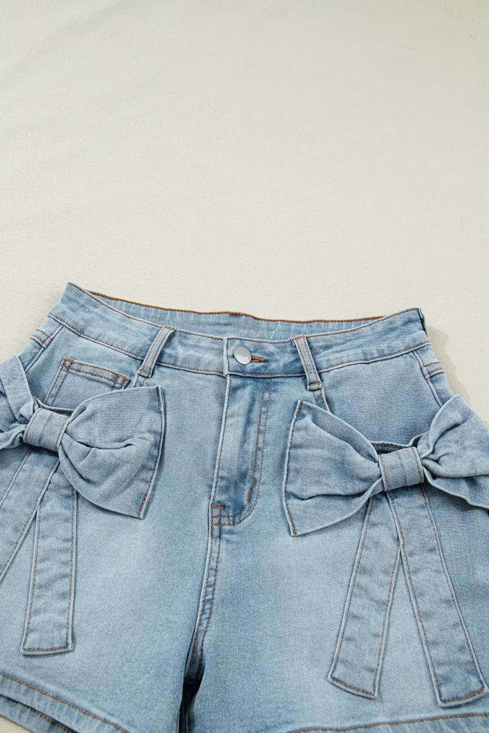 Light blue denim shorts with bow details on a beige background