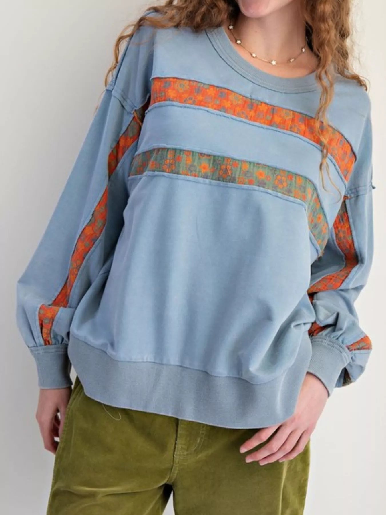 Light blue sweatshirt with orange and green pattern worn by a person on a white background