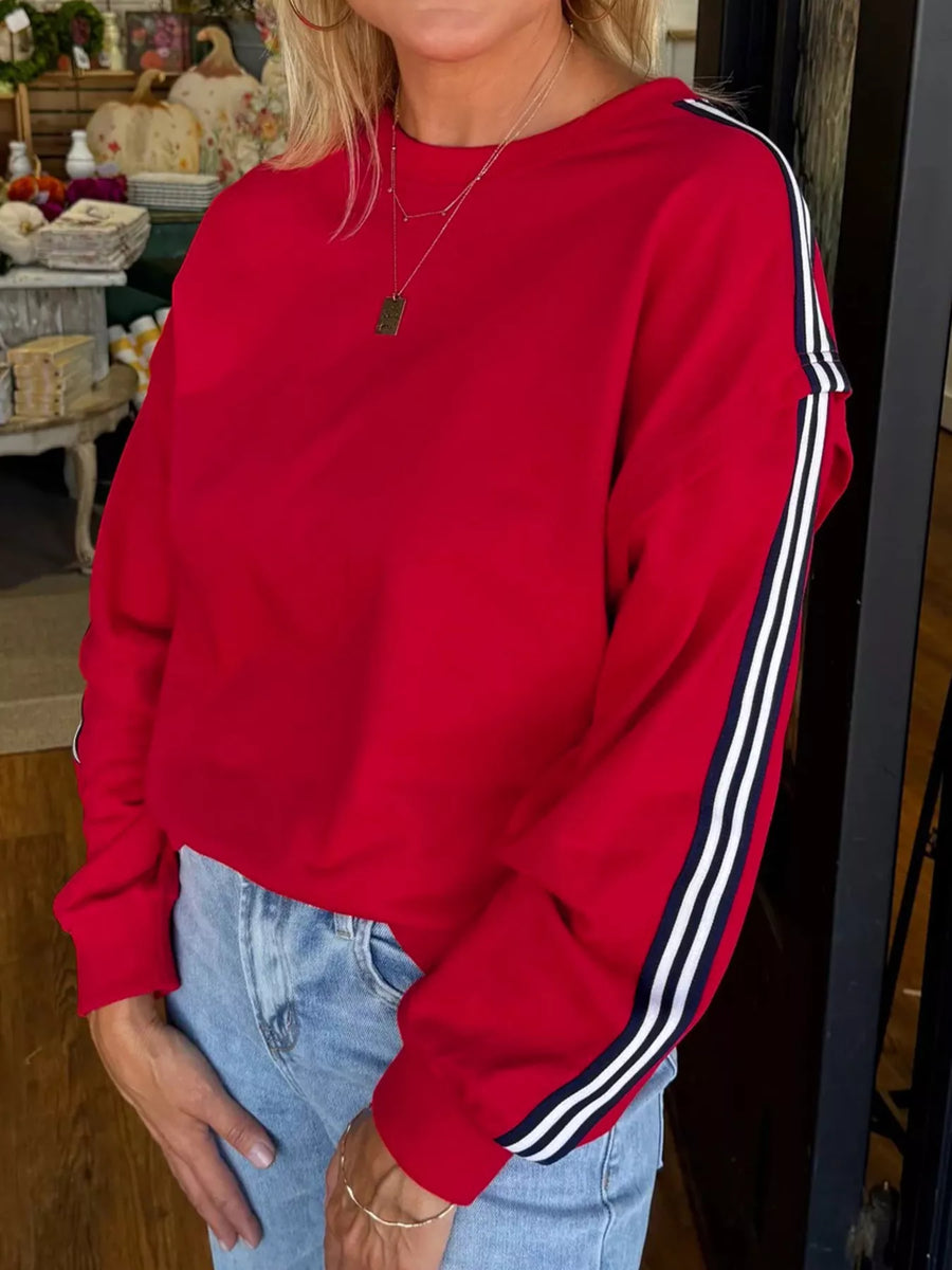 Person wearing a red sweatshirt with white stripes on a blurred indoor background