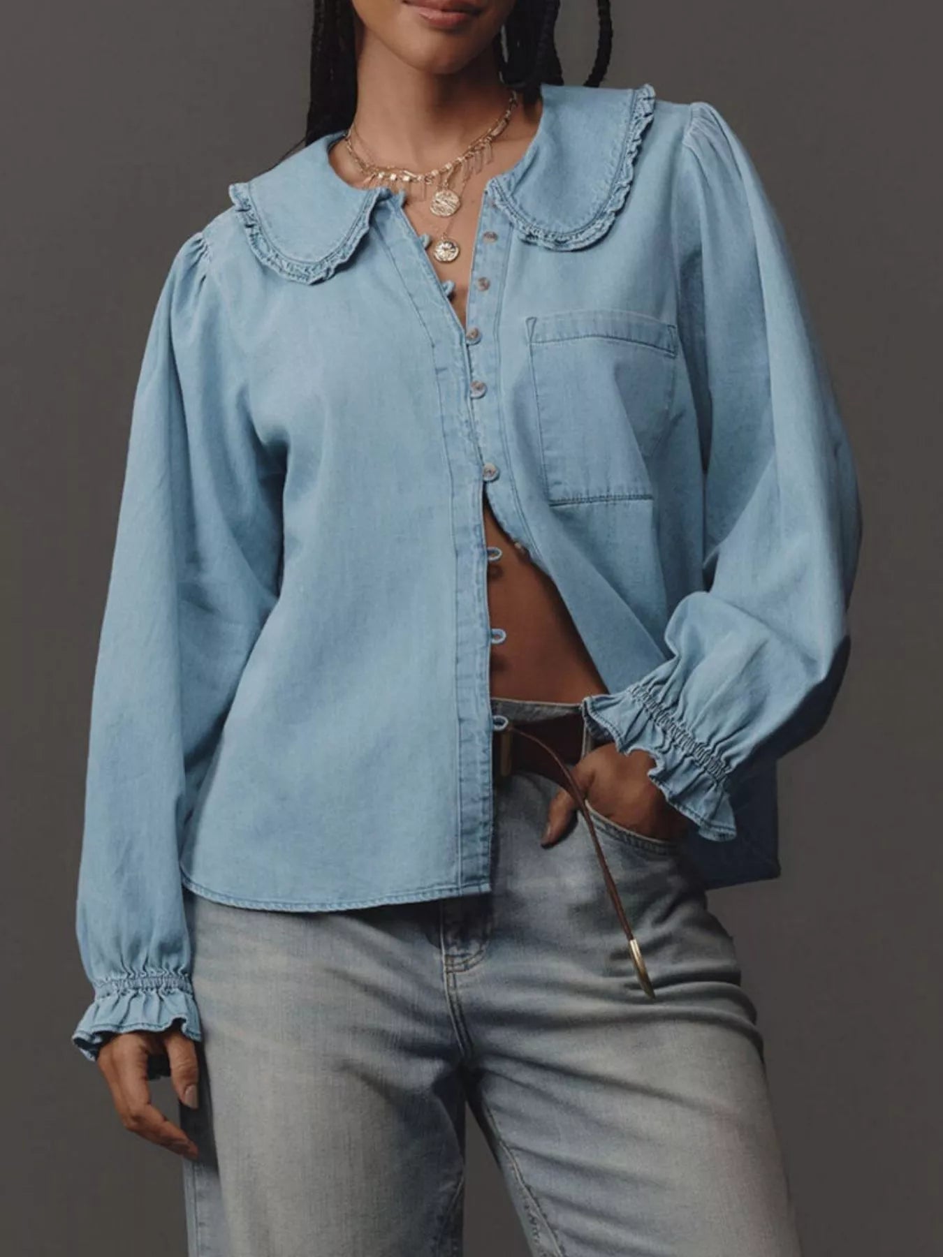 Person wearing a light blue denim shirt with ruffled collar and gray jeans on a dark background