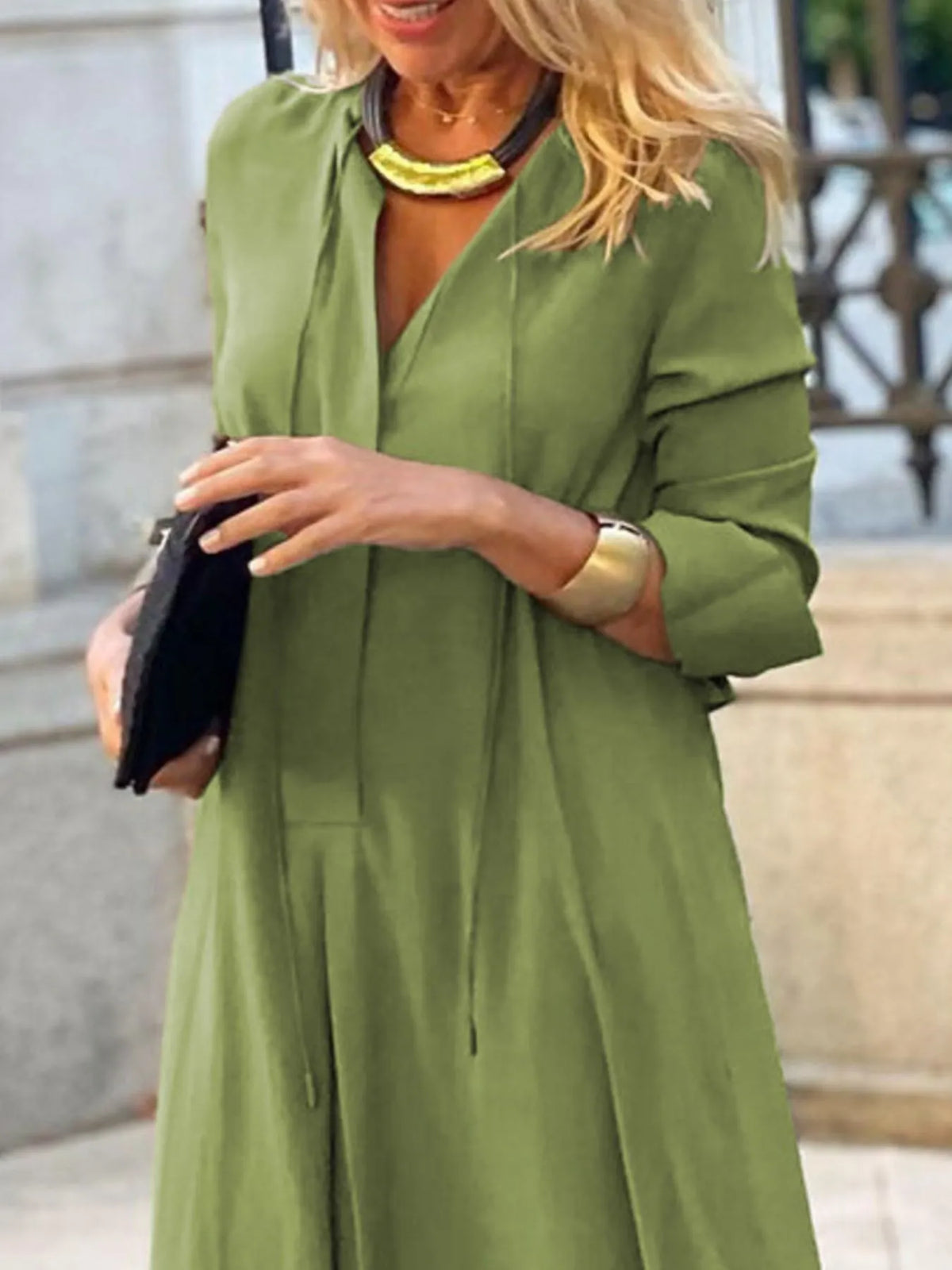 Woman wearing a green dress holding a black clutch outdoors.
