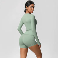 Woman wearing a green long-sleeve top and shorts set on a light gray background